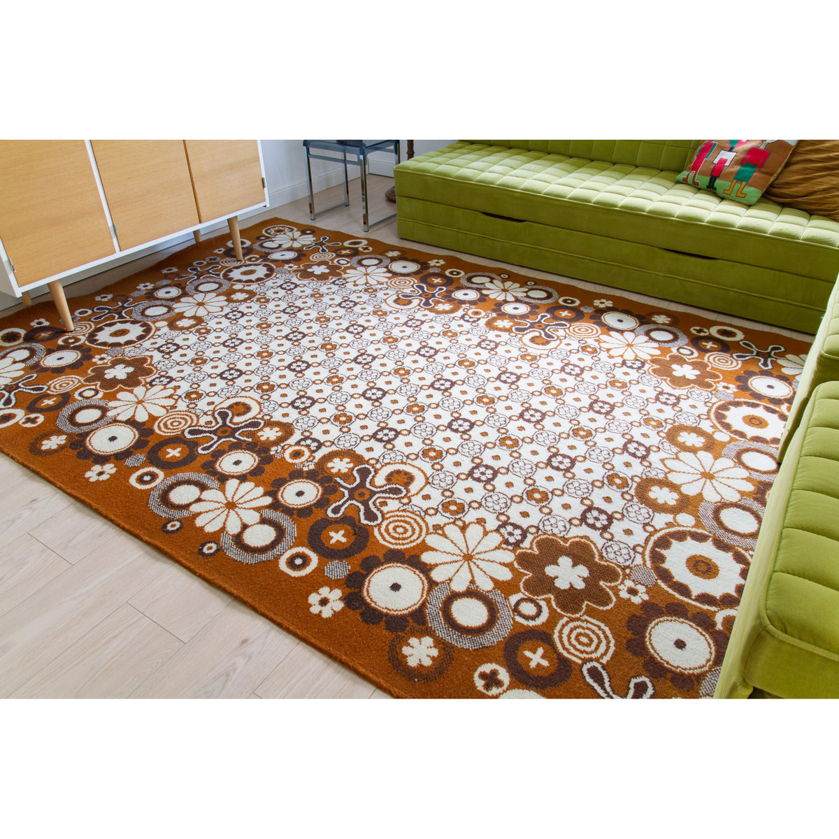 Top wide-angle view of a large 70s area rug in caramel, brown and ivory in a retro themed living room with wooden sideboard and lime green modular sofa