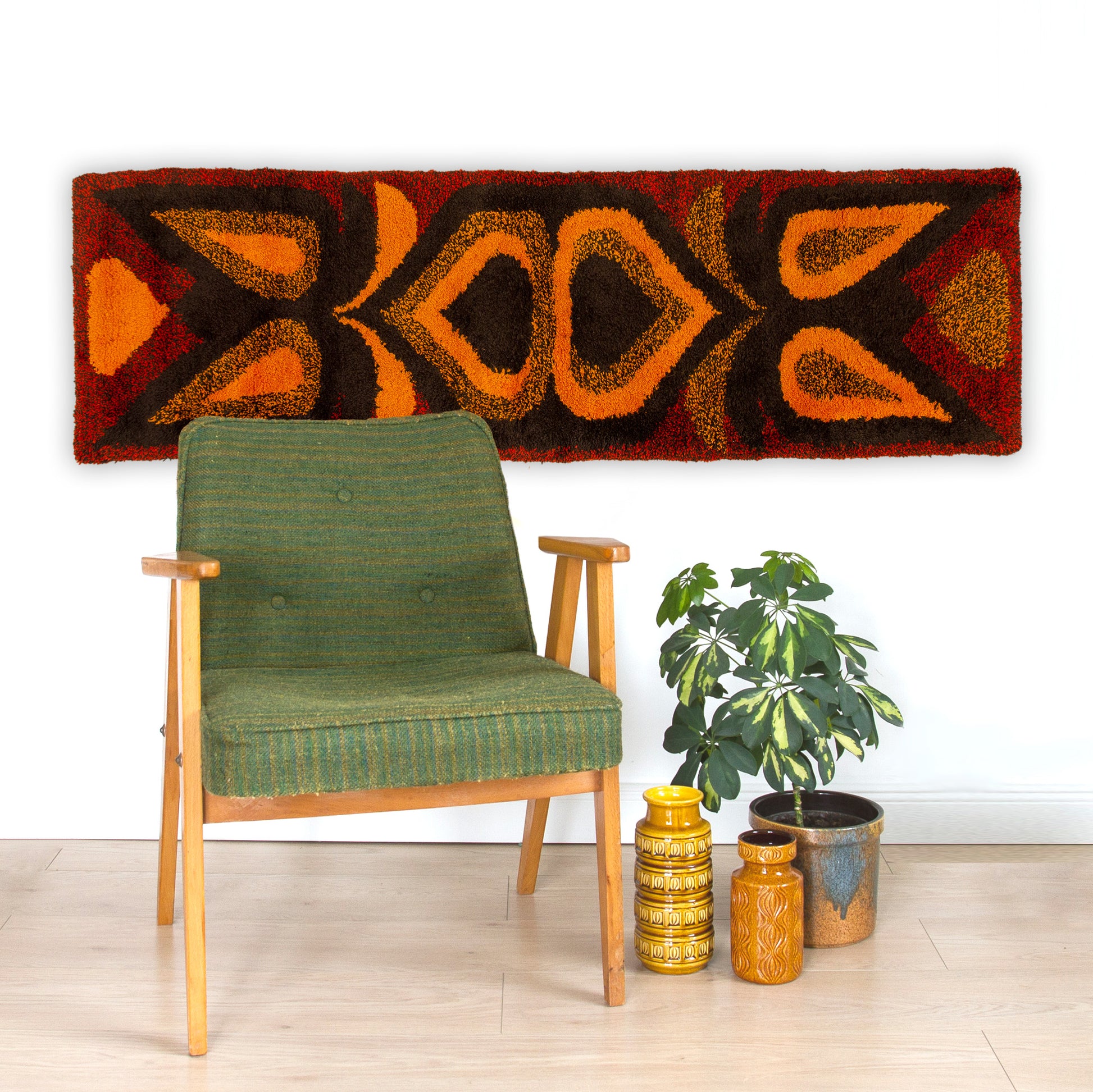 A horizontal 68-inch mid century modern geometric tapestry hung majestically over a green retro armchair, bringing warm acoustic dampening to a room.