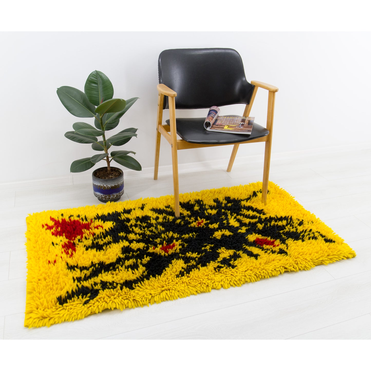 Bold yellow vintage mid-century tapestry styled as an accent floor rug, demonstrating one possible use of this multi-purpose rug. The modern black lounge chair and indoor plant shows scale and vibrant colors.
