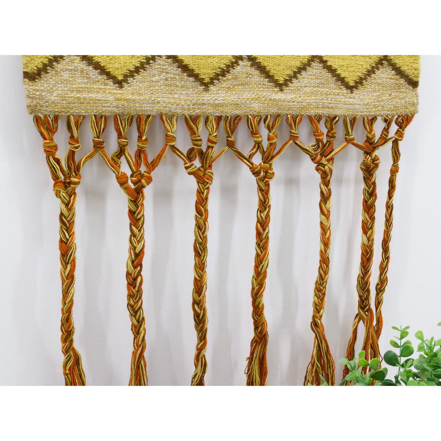 Detailed close-up photo of the intricate long braided wool fringes bordering the bottom edge of a mid century modernist hungarian tapestry.