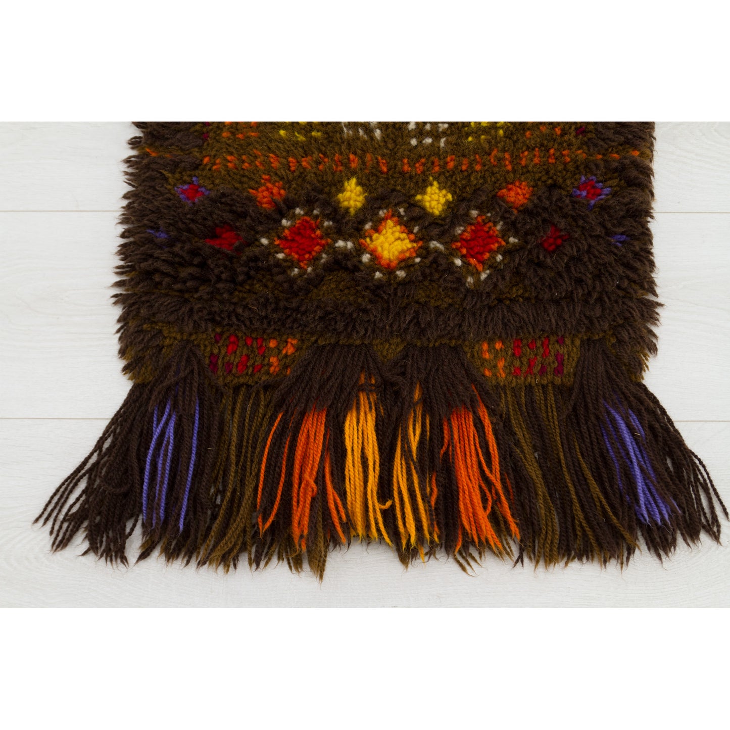Detailed close up focusing purely on the long, thick, multi-colored yarn fringes falling elegantly from the bottom edge of the vintage mid-century wall hanging.