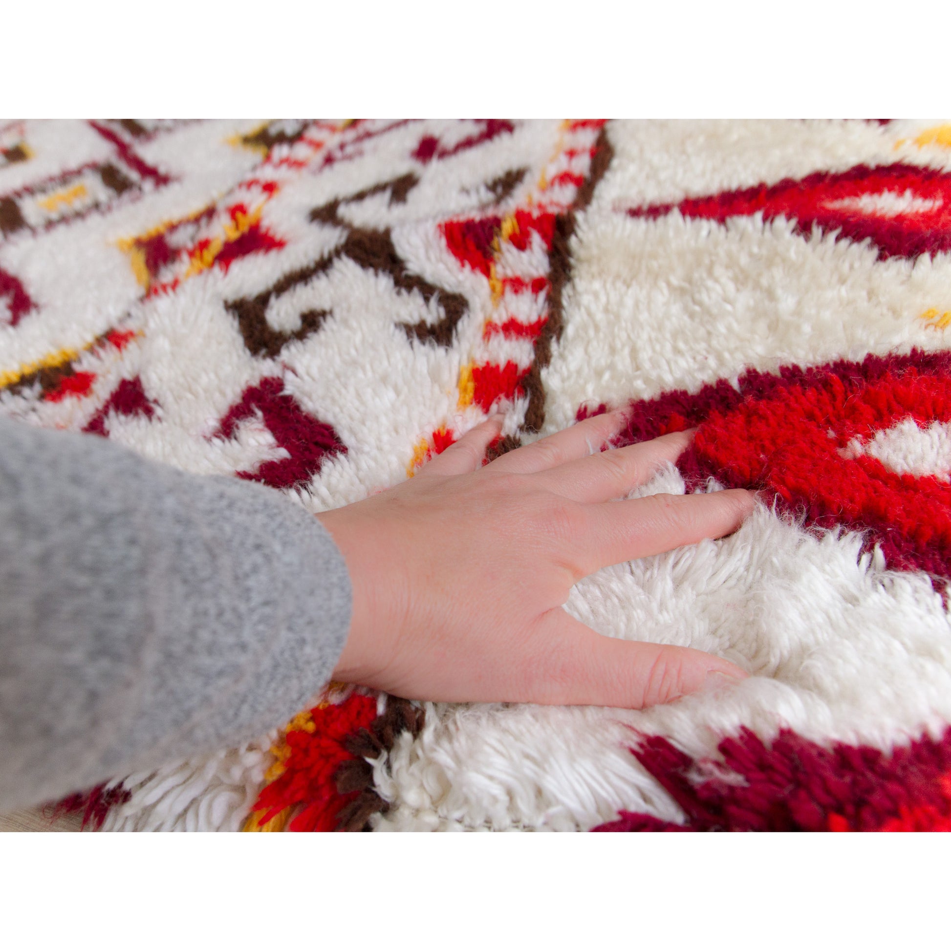 A hand hovering gently over the vibrant, incredibly cozy, and deeply soft cotton pile surface of the large mid-century geometric tapestry.