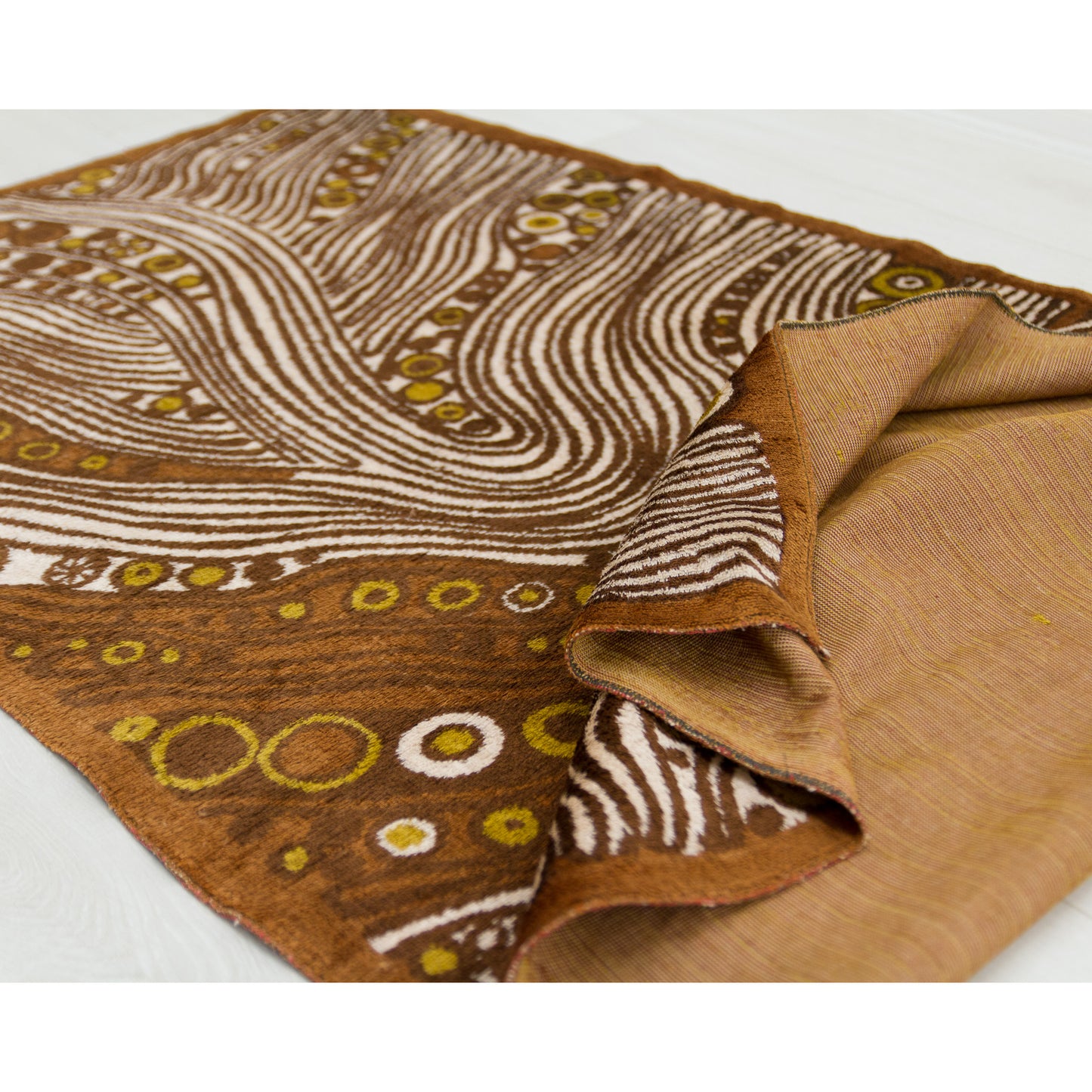 Angled photograph emphasizing the durability and striking visual impact of the heavy-weight moquette textile. Deep chocolate browns and glowing ochre waves catch the room's lighting.