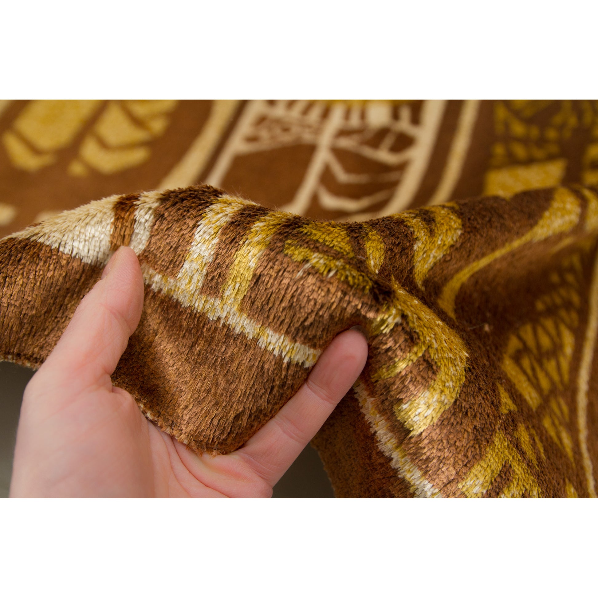 Hand holding the tapestry edge to demonstrate the gentle shimmering and flexibility of the vintage moquette pile. Rich, velvety texture in warm earth tones.