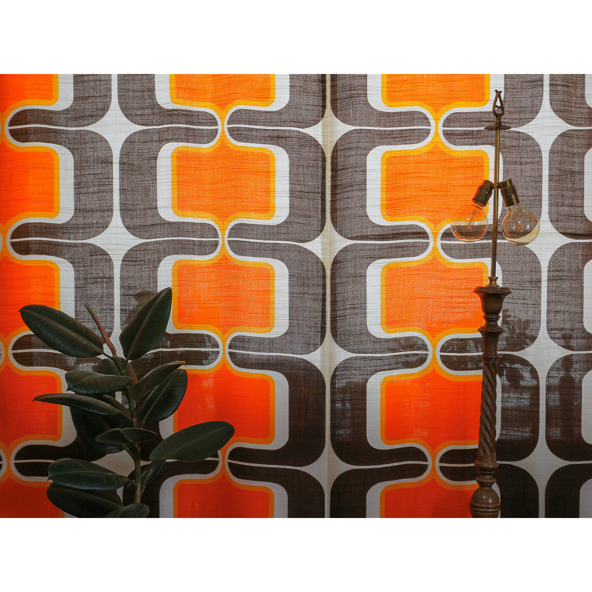 Retro - Space Age style curtain panels behind a vintage brass lamp, warm orange and brown pattern glowing in the light.