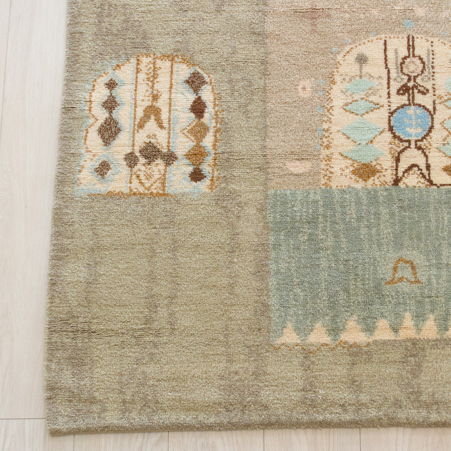 Bottom left quarter showing thick hand-knotted fine wool piles on a cotton foundation. Muted neutral beige and brown abstract wall tapestry details.