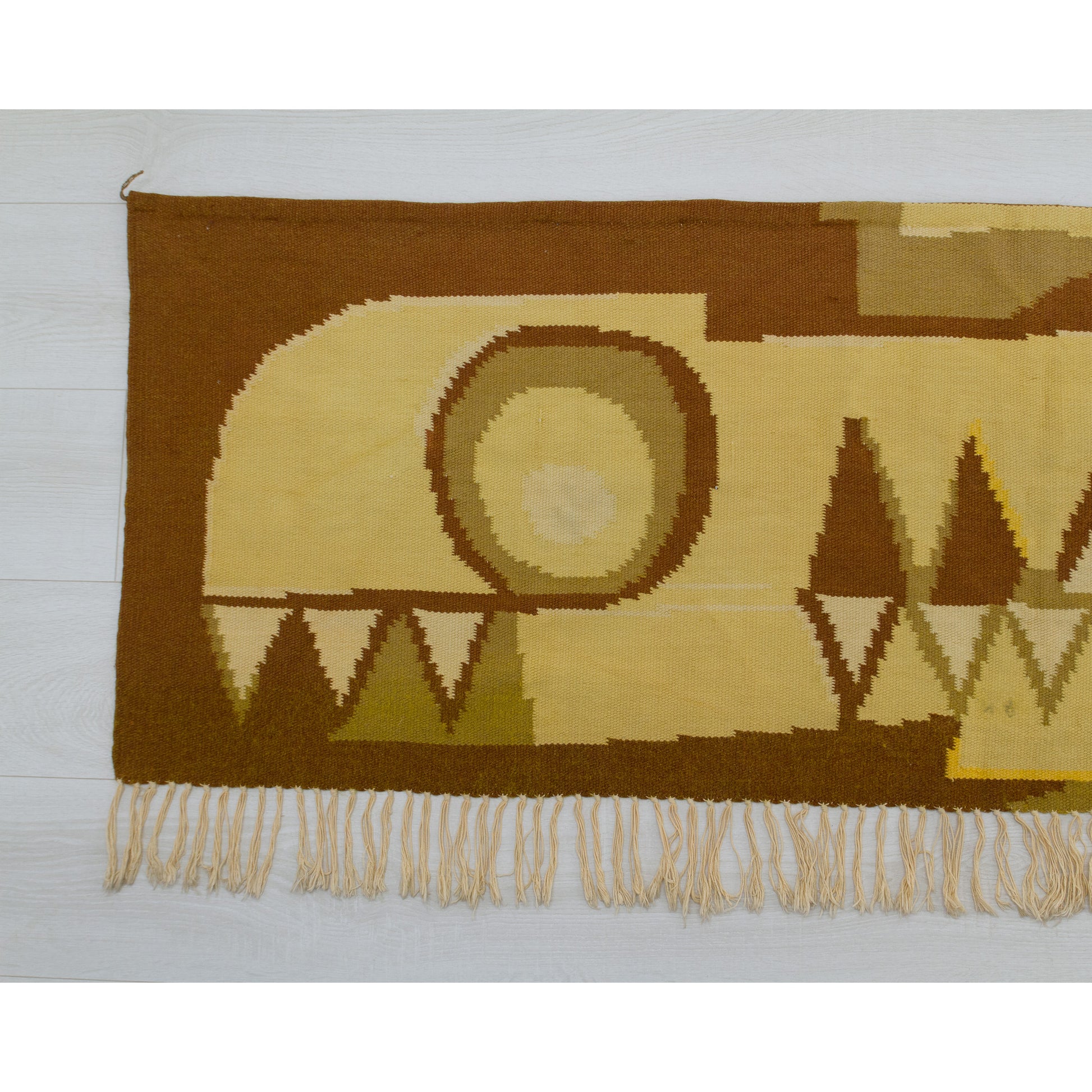 Left section of the woven wall hanging displaying abstract circular motifs and jagged triangular patterns in warm autumn 70s tones.