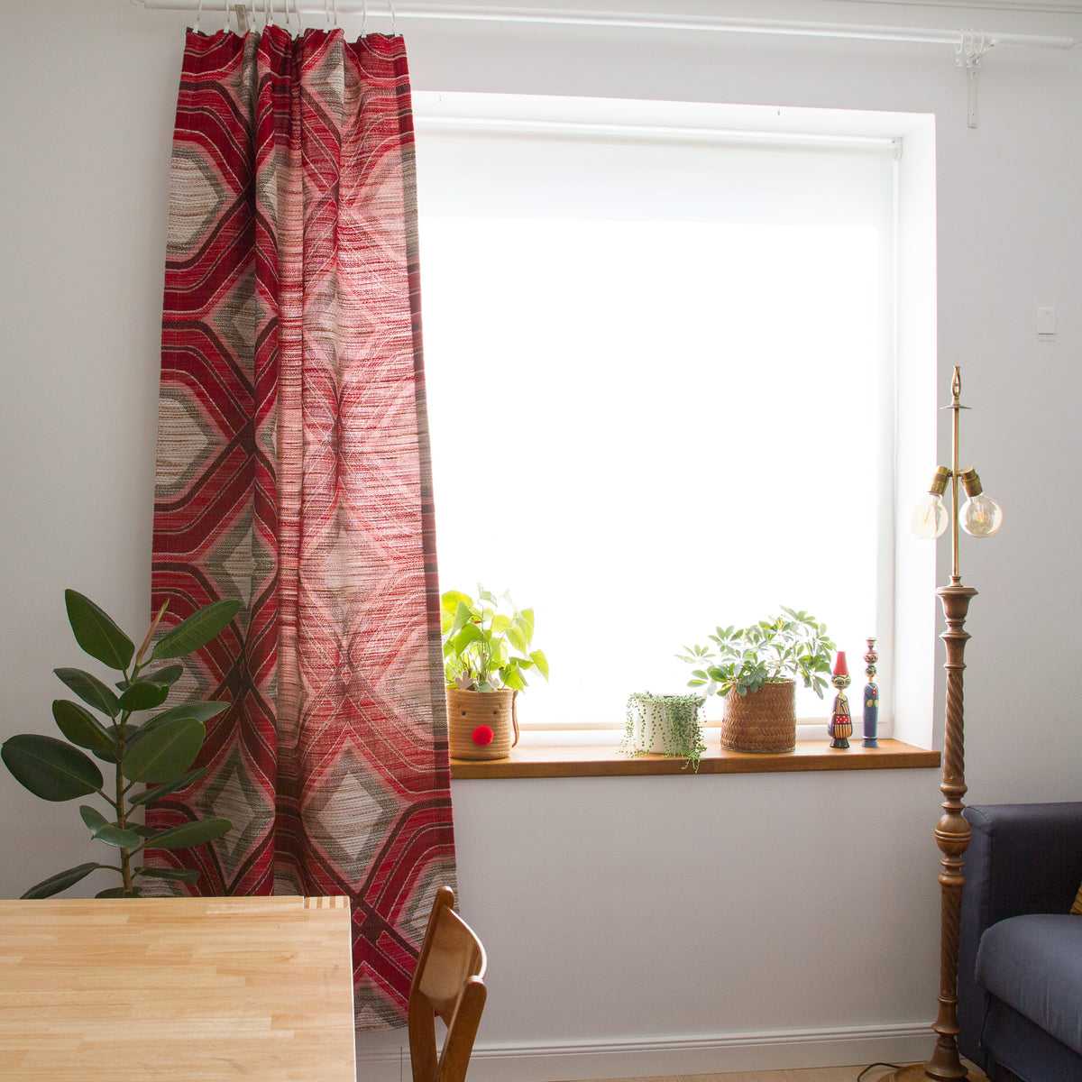 Mid century style red geometric curtain hanging next to a bright window with plants, creating a retro 70s style living room interior