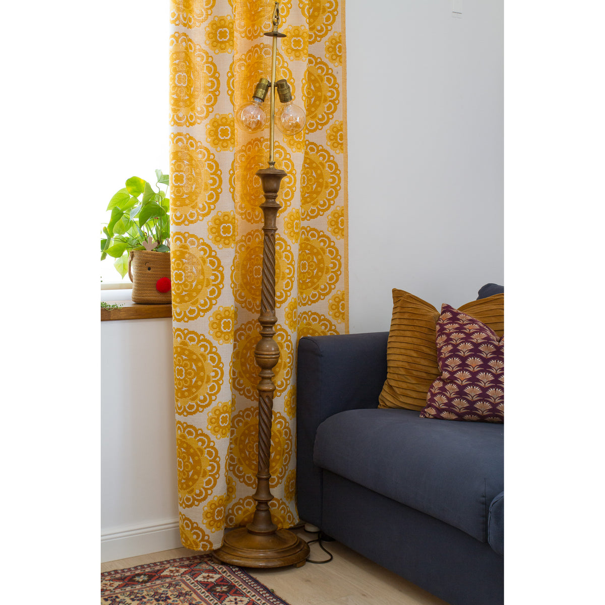 Full length mid century yellow curtain panel next to window with green plants and wooden floor lamp.