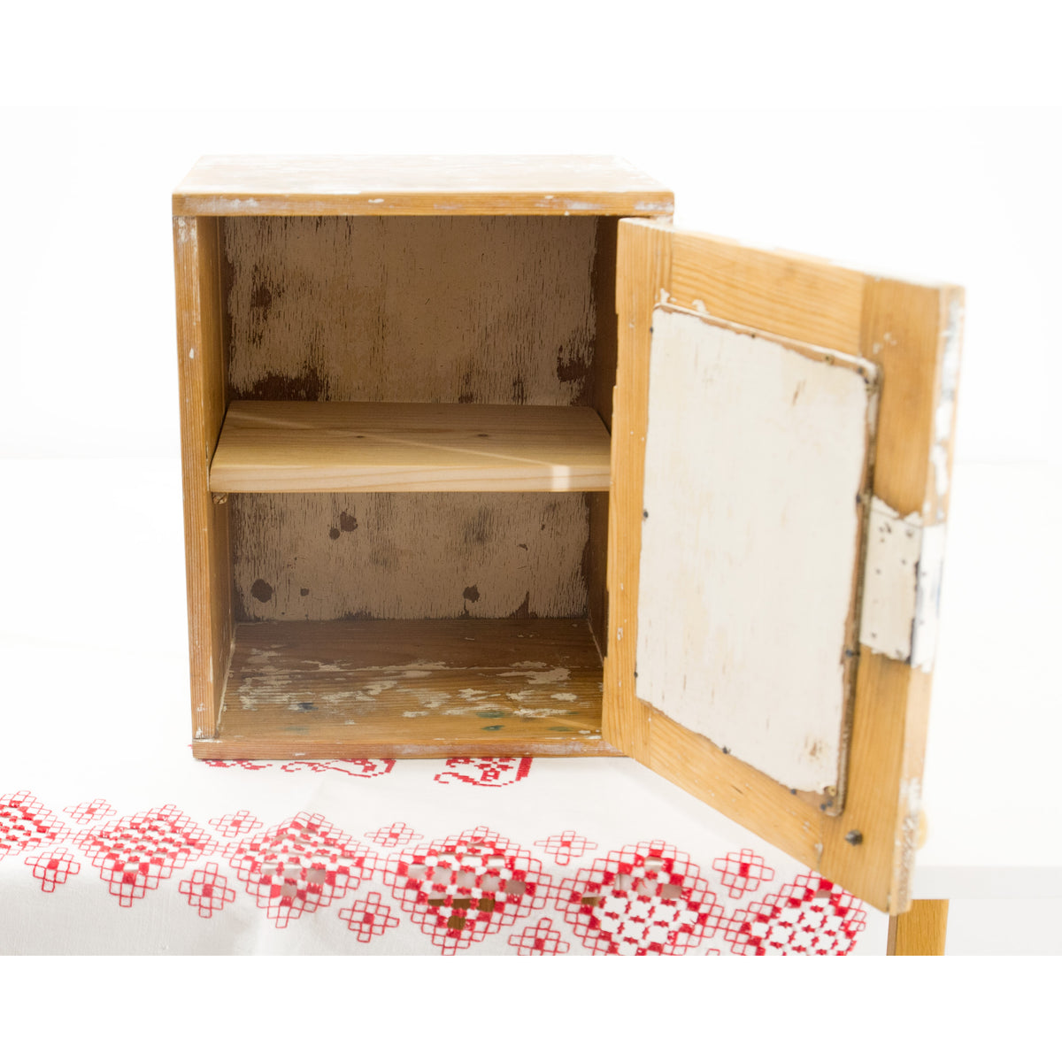 A small rustic wall cabinet with a distressed finish, featuring a single shelf and an open door with peeling white paint, with a bold antiqhe farmhouse style.