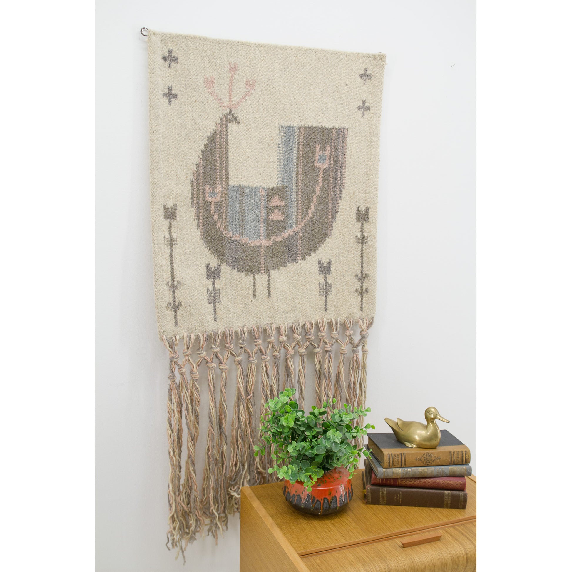 An angled, close-up lifestyle view of an authentic vintage Eva Nemeth wool wall hanging featuring an incredibly calming, pastel bird motif and extra-long tassels.