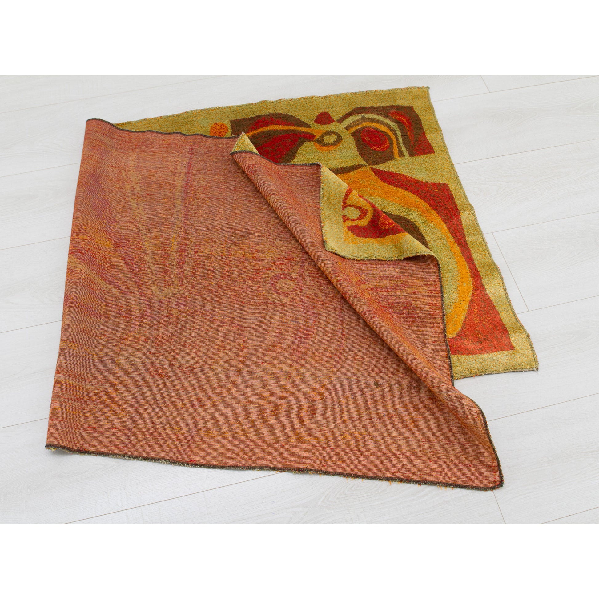 The tapestry folded and gently draped on the floor, highlighting the contrast between the mid-century modern abstract patterns and the muted red backing.