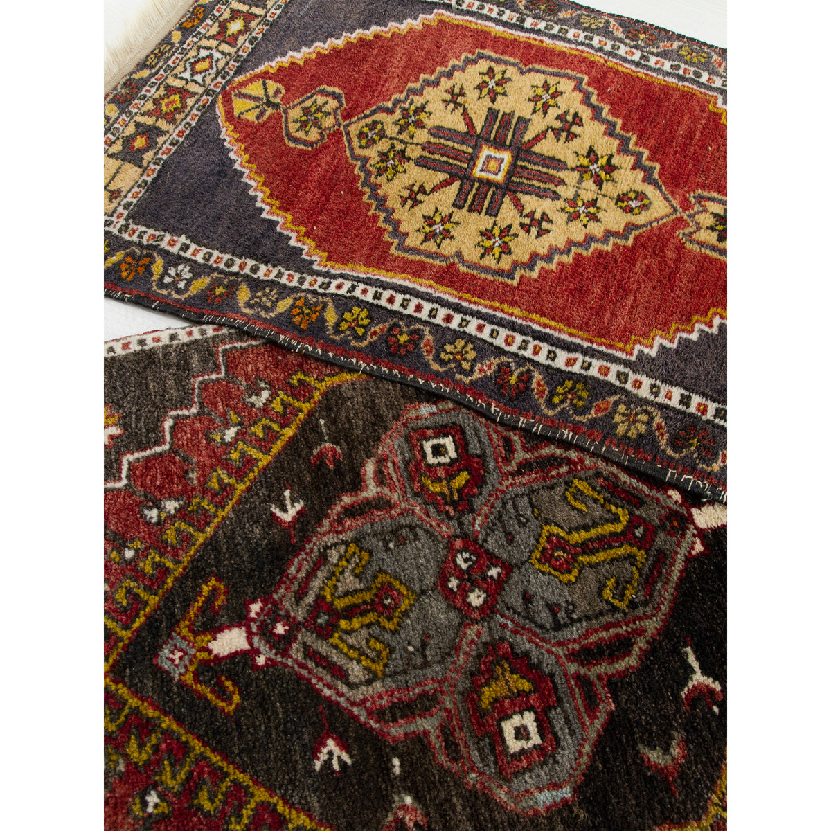 A pair of vintage Turkish rugs overlapping, one red and gold, one chocolate brown with grey and mustard