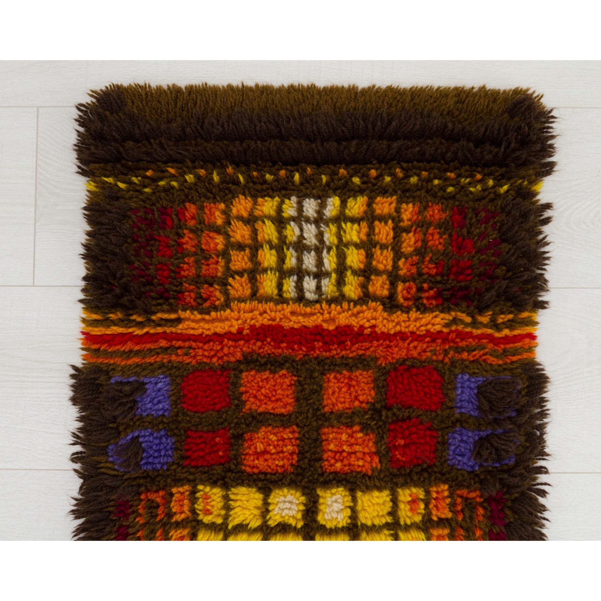 Close up photography of the top half of the geometric rya rug, showing perfectly aligned, colorful cotton piles in a 1970s brutalist style grid.