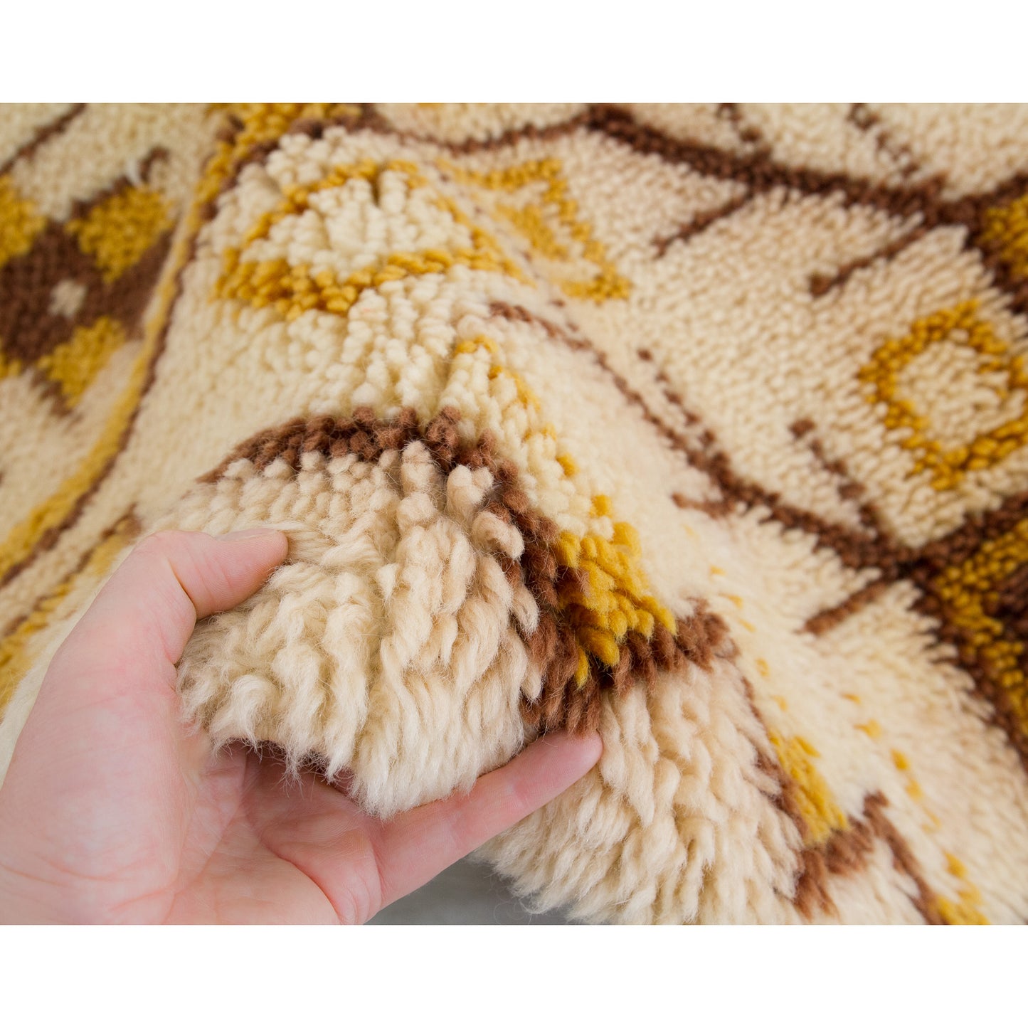 A hand lifting a fold of the incredibly soft 1970s wall art to clearly demonstrate the tactile thickness of the one-inch deep retro wool piles.