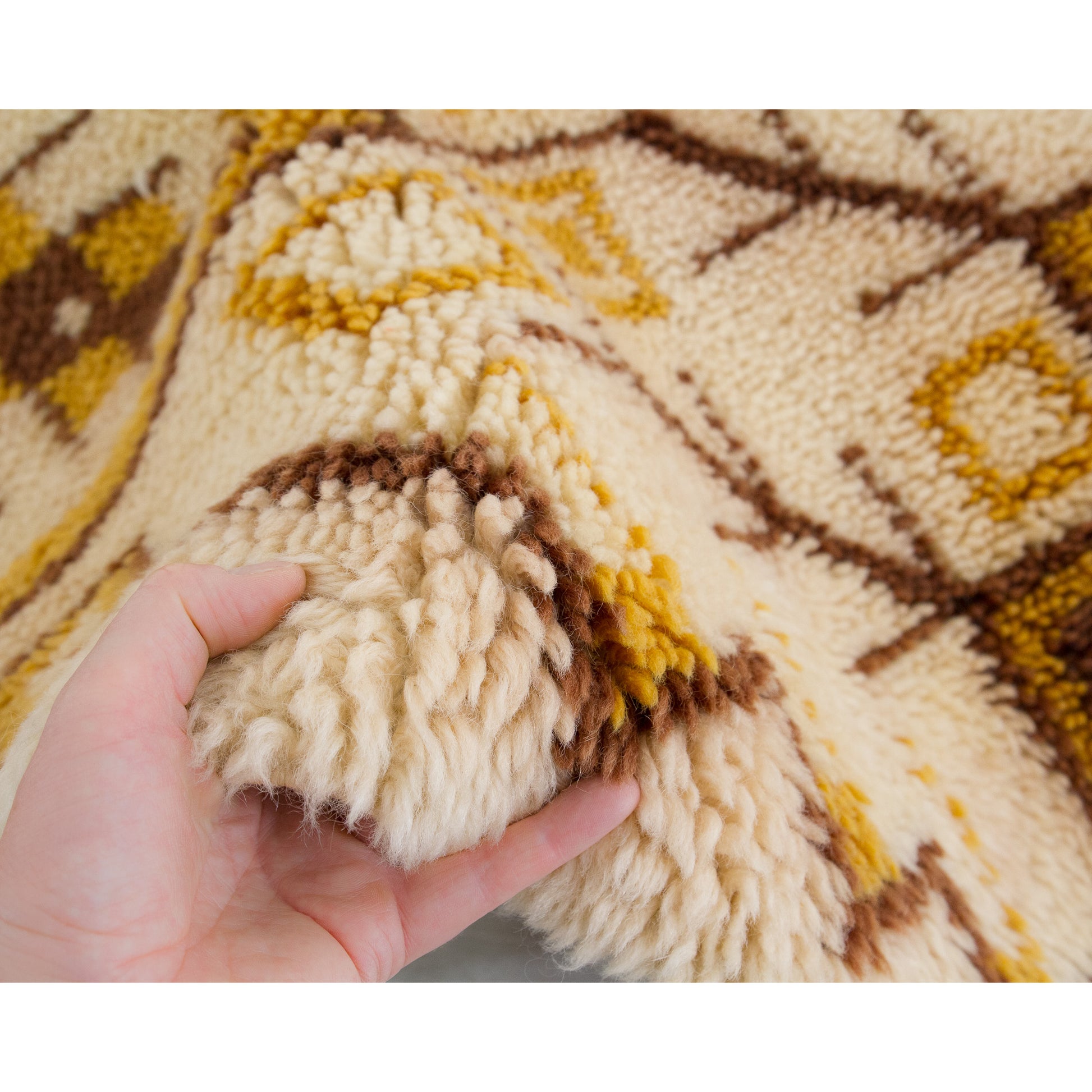 A hand lifting a fold of the incredibly soft 1970s wall art to clearly demonstrate the tactile thickness of the one-inch deep retro wool piles.