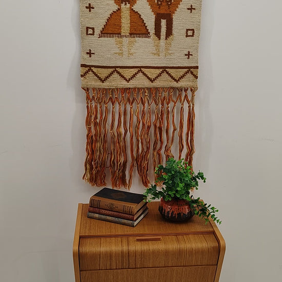 A brief video showcasing a vintage 70s orange and brown geometric tapestry. The textile is gently draped and folded in-hand to highlight the flexible, heavy handwoven quality and warm aesthetic earth tones.