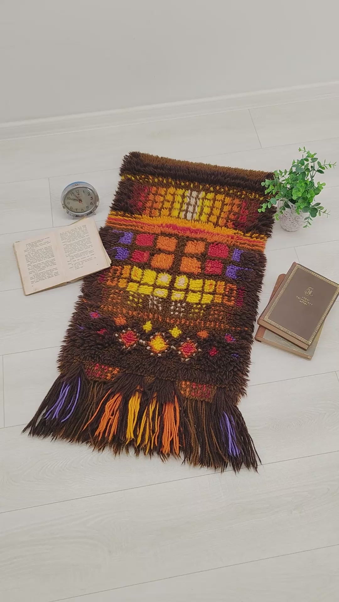 A sweeping video panning over a vintage 70s orange and brown geometric Smyrnafix long pile rug, with hands manipulating the dense, colorful shag fibers to show thickness and lush texture.