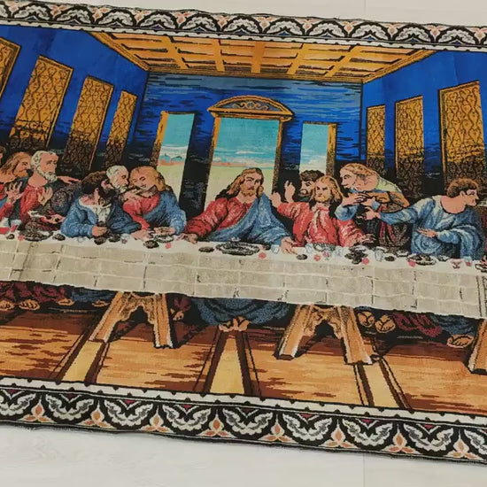 A detailed video sweeping over the majestic scale of a vibrant cobalt blue Last Supper tapestry. A hand touches and folds the fabric, demonstrating the soft, velvet-like moquette pile.
