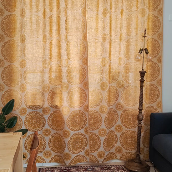 Video of a 70s vintage mustard yellow jacquard curtain pair with woven medallion pattern, showing the full length curtains hanging at a window and close-ups of the reversible textured fabric.