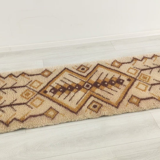 A short video panning over the vintage wool rug, demonstrating the symmetrical geometric design and mellow earthy colors. The rug is being touched and squeezed to show the soft, pliable structure of the multi-purpose rug.
