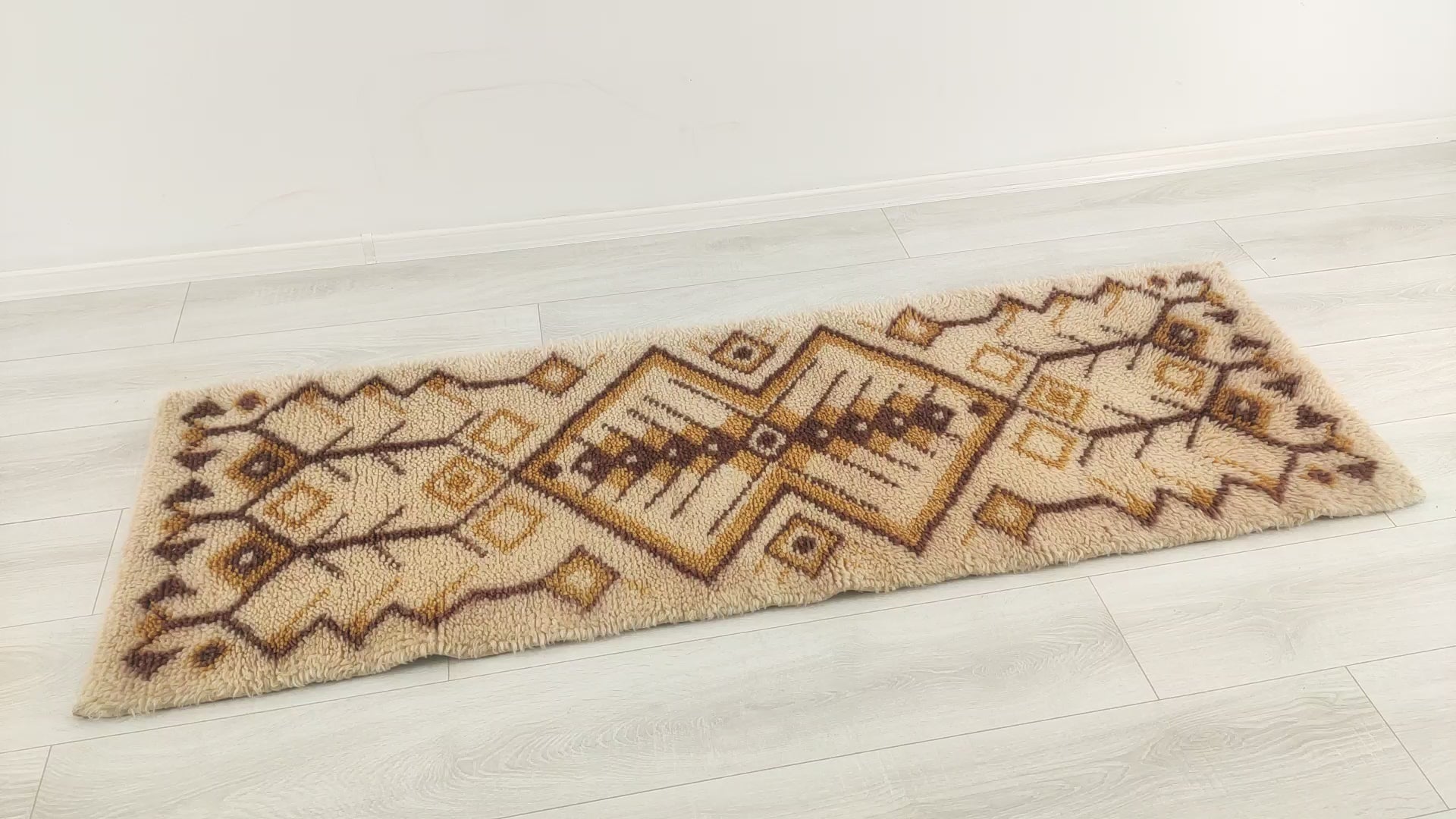 A short video panning over the vintage wool rug, demonstrating the symmetrical geometric design and mellow earthy colors. The rug is being touched and squeezed to show the soft, pliable structure of the multi-purpose rug.