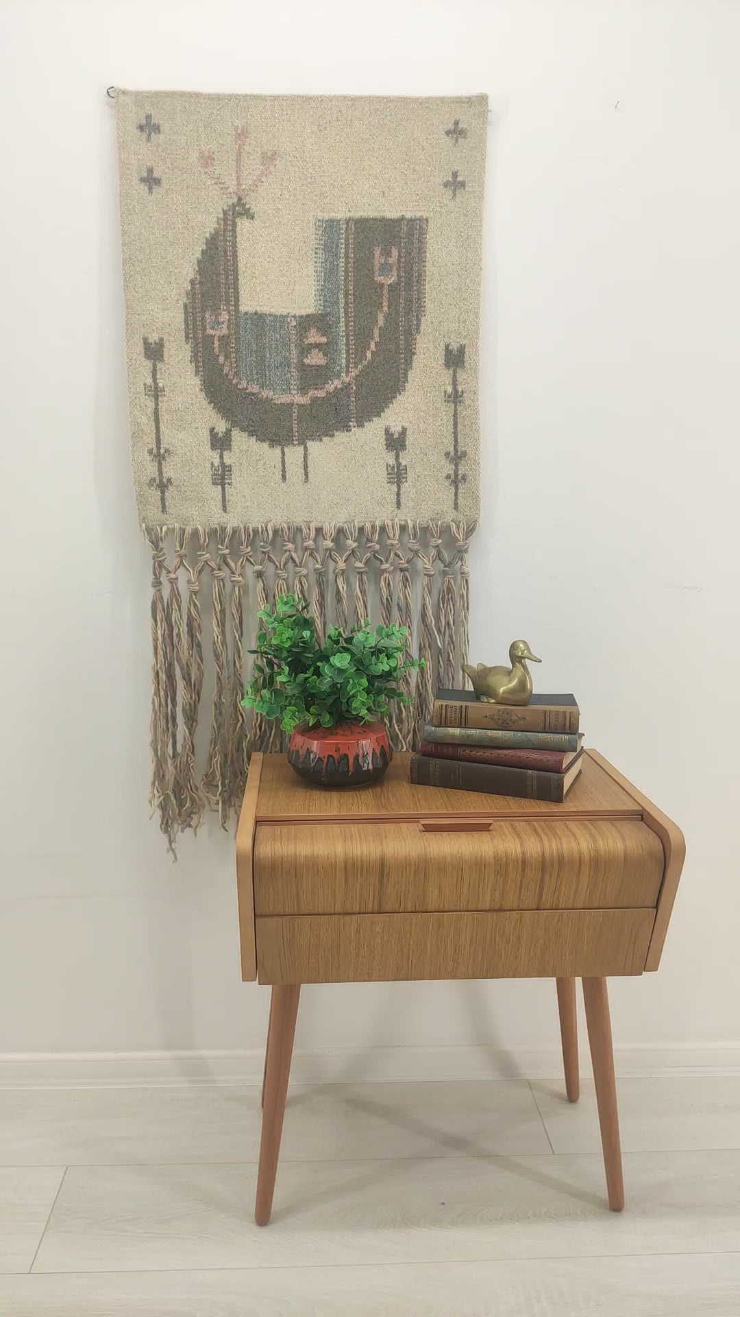 Slow panning video of the stunning pastel bird tapestry on a bright wall, followed by a hand rubbing the smooth flatwoven wool texture to showcase the tactile coziness of the material.