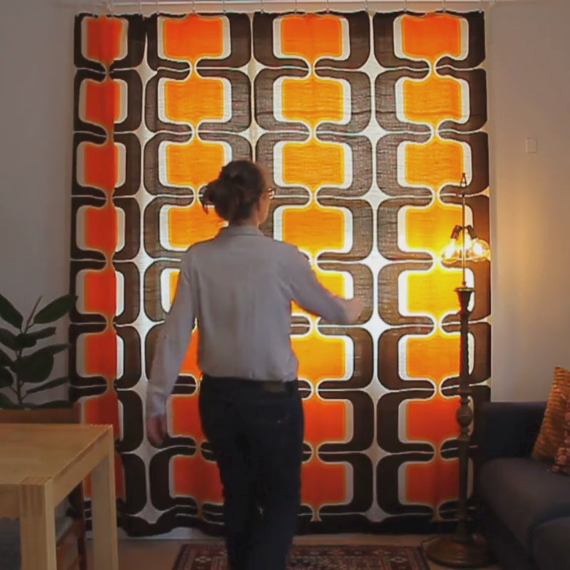 Video of a 60s vintage curtain pair with orange, brown and cream geometric pattern, showing the full length curtain hanging at a window and close-ups of the textured semi-sheer fabric.