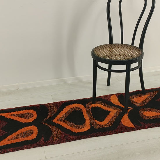 Video smoothly panning from top to bottom across the deep-pile orange retro tapestry. Hands handle the rug, showing its satisfying weight, thick tufted yarns, and premium durability.