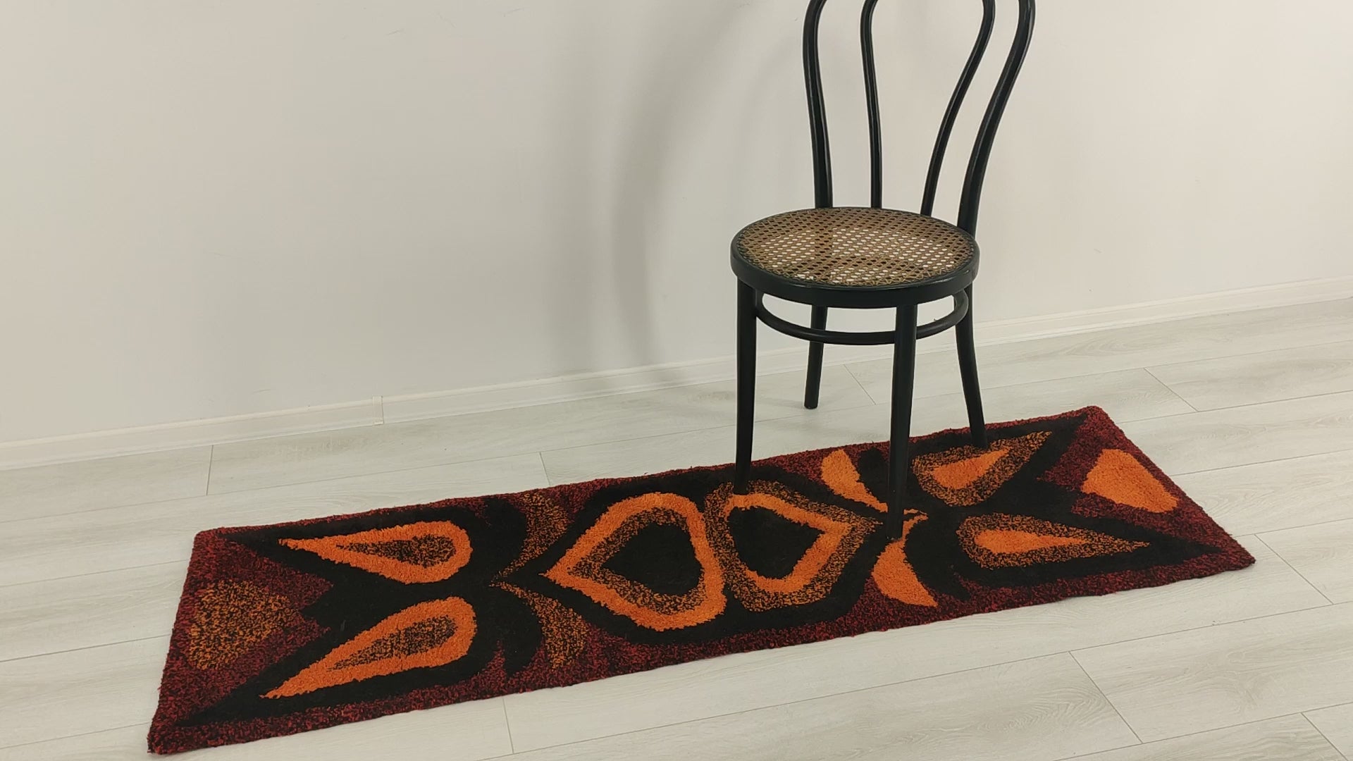 Video smoothly panning from top to bottom across the deep-pile orange retro tapestry. Hands handle the rug, showing its satisfying weight, thick tufted yarns, and premium durability.