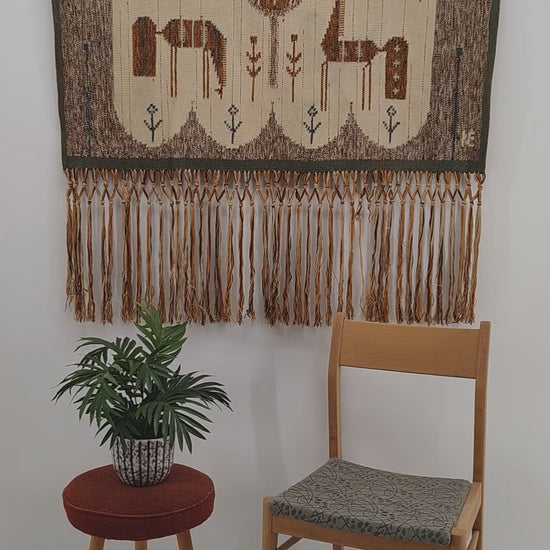 A short video showing a hand gently folding, touching, and demonstrating the dense flatwoven wool texture and softly draping fringes of a 1970s Eva Nemeth horse tapestry.
