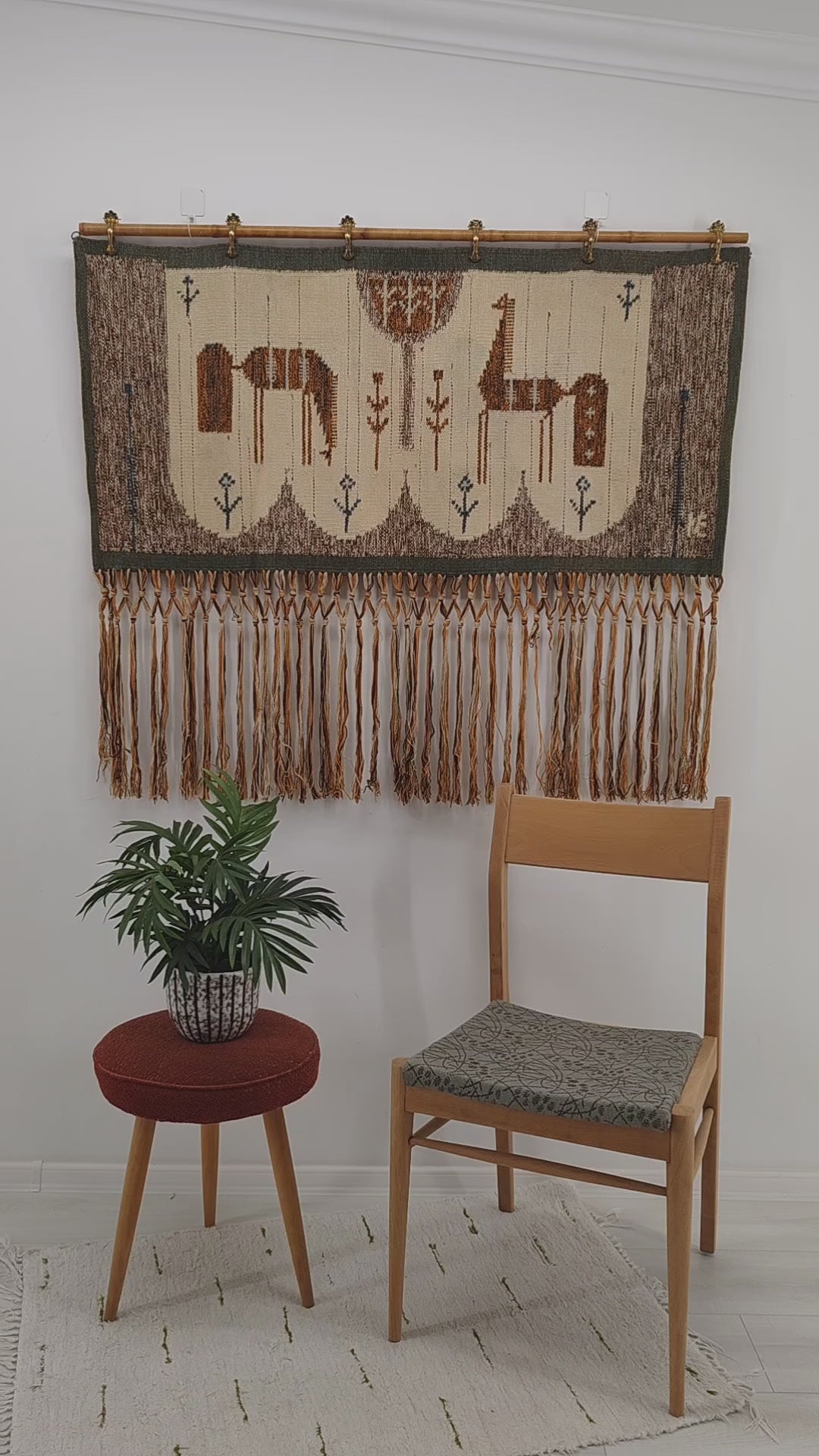 A short video showing a hand gently folding, touching, and demonstrating the dense flatwoven wool texture and softly draping fringes of a 1970s Eva Nemeth horse tapestry.