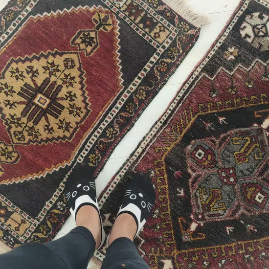 Close look at two small vintage Turkish yastik rugs, showing their colors, tribal patterns and hand-knotted wool pile.
