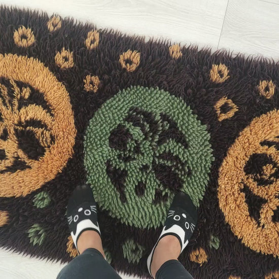 A smooth, satisfying short video where hands gently rub, fold, and caress the dark brown, yellow, and mint cotton piles of a 1970s vintage shag runner rug, showcasing exceptional softness.