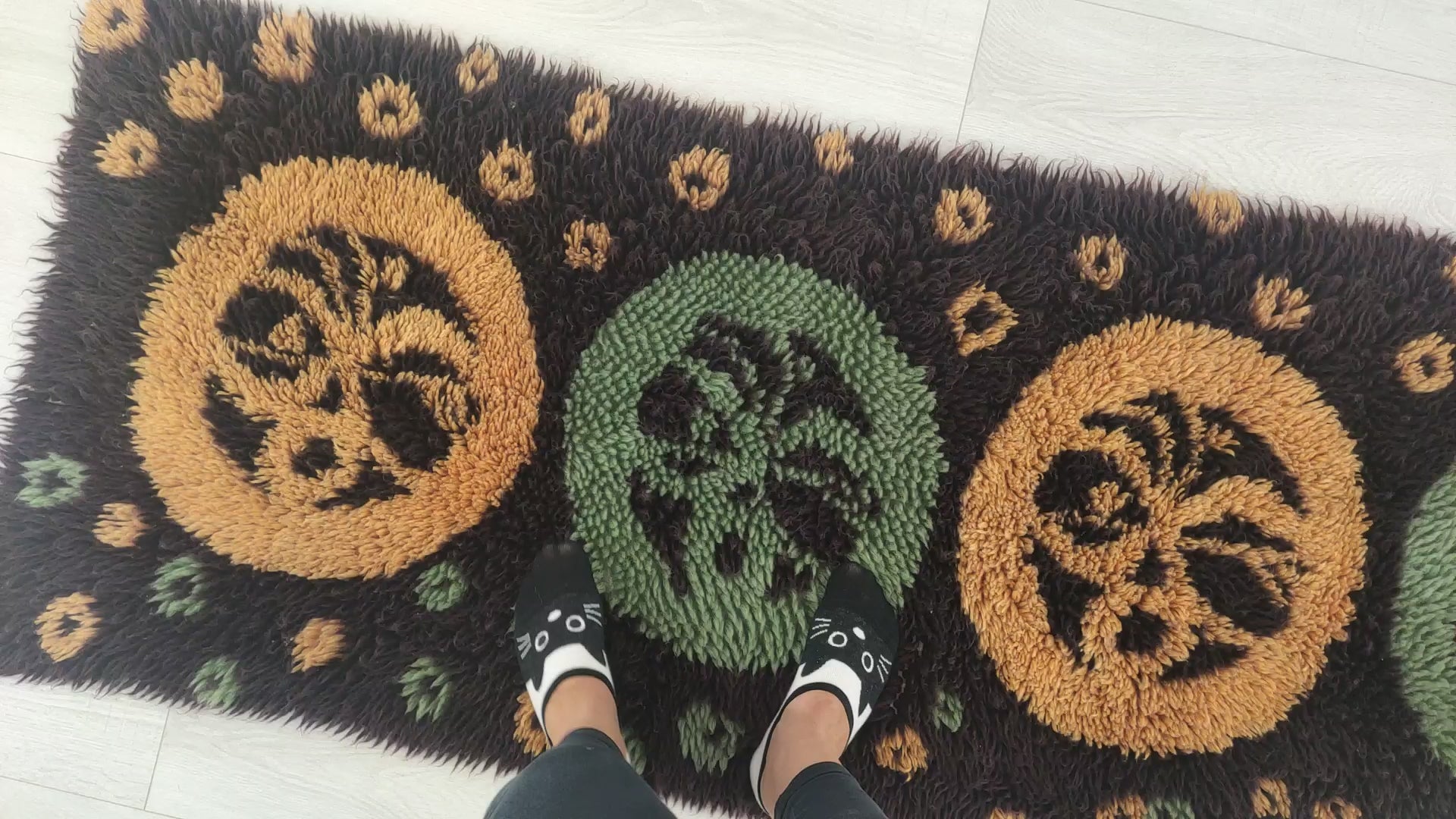 A smooth, satisfying short video where hands gently rub, fold, and caress the dark brown, yellow, and mint cotton piles of a 1970s vintage shag runner rug, showcasing exceptional softness.