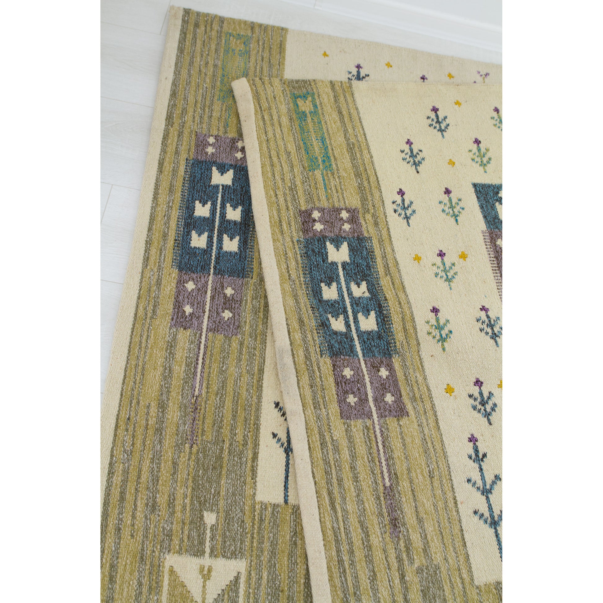 Close up focusing on the neatly finished and cleanly hemmed edge of the mid-century handwoven flatweave rug.