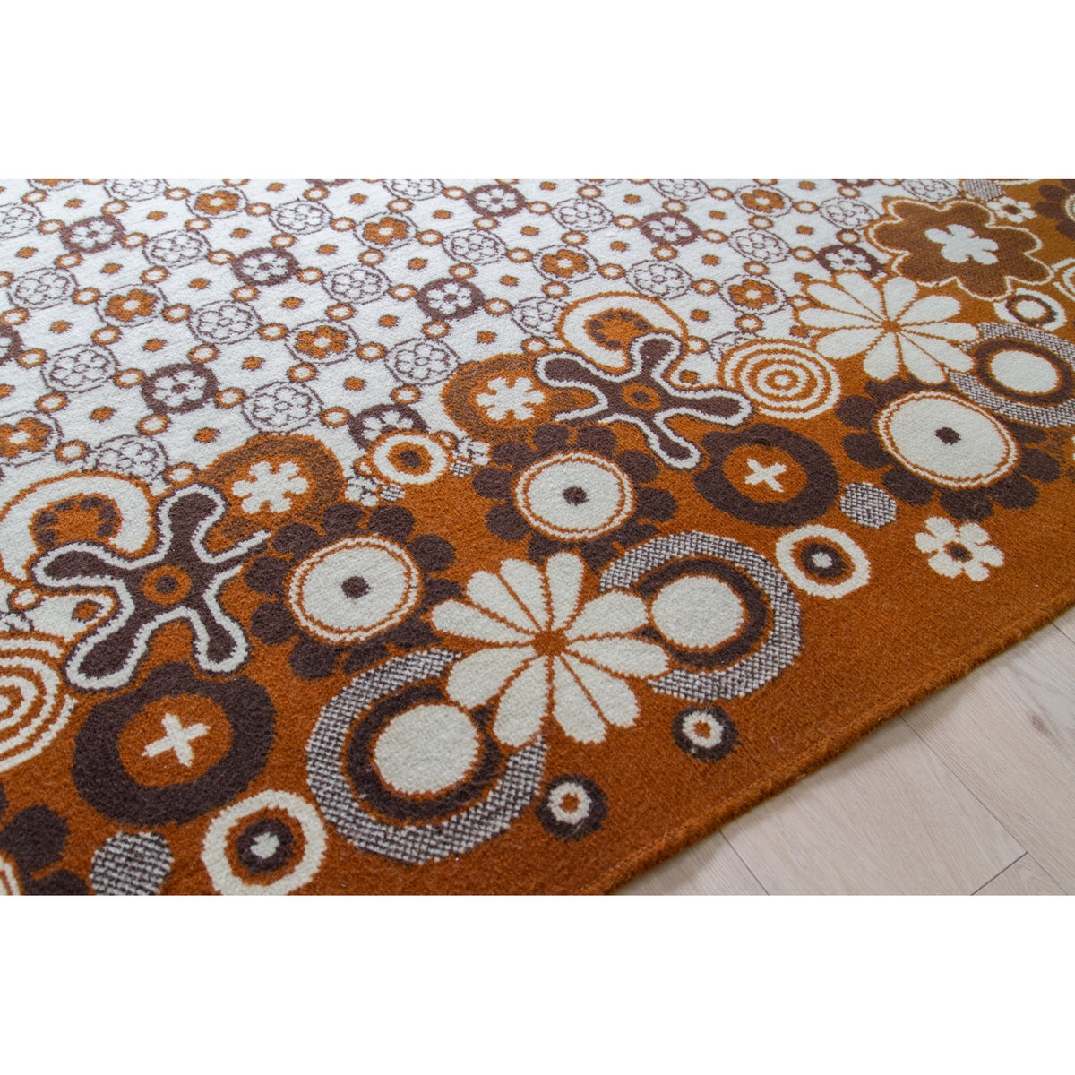 Close-up of psychedelic rug pattern with daisies, bullseye circles and star flowers in caramel, brown and ivory, also showing the neat and damage-free edges of the rug.