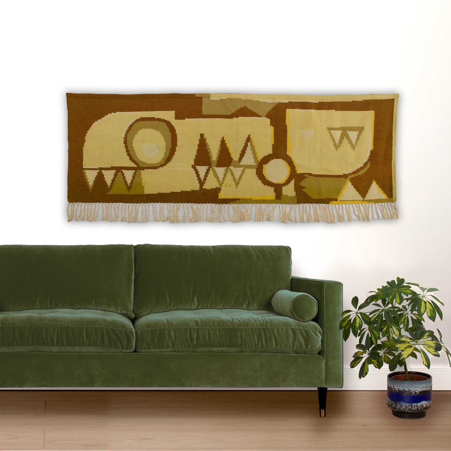 Mockup showing the earthy fringed woven wall hanging providing striking visual warmth above an emerald green mid-century modern couch.