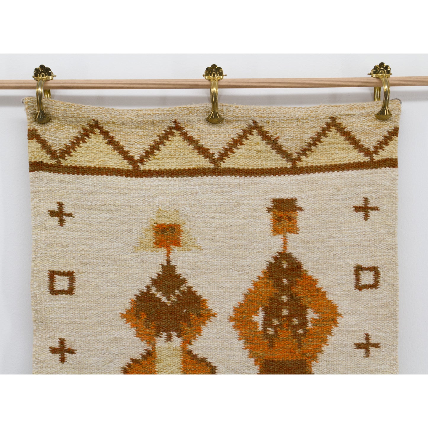 Close up photography of the handwoven tapestry showcasing beige, brown, and orange wool yarns depicting zigzags, geometric crosses, and highly stylized abstract human figures.