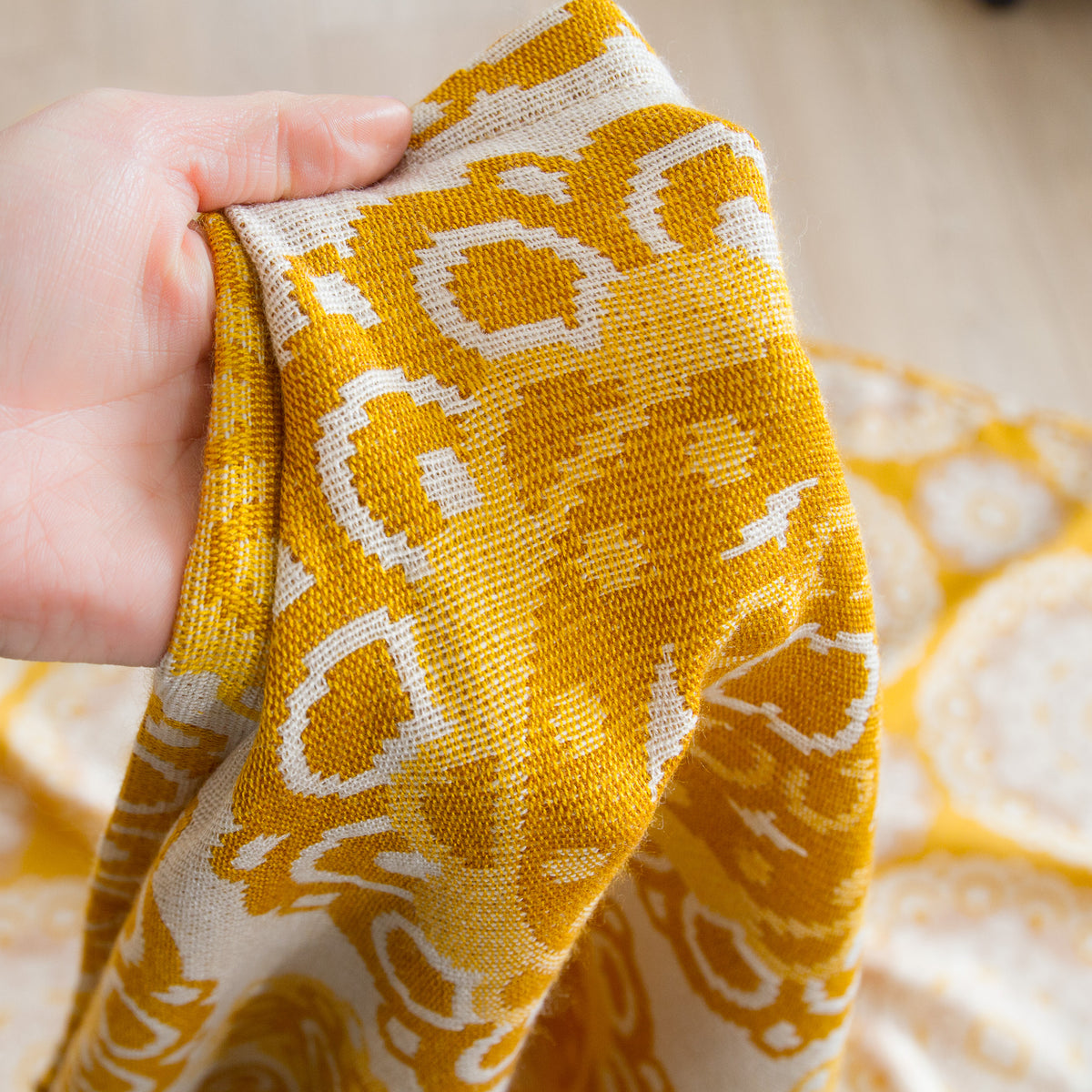 Hand holding a vintage woven curtain fabric, showing the texture of the mustard yellow jacquard textile