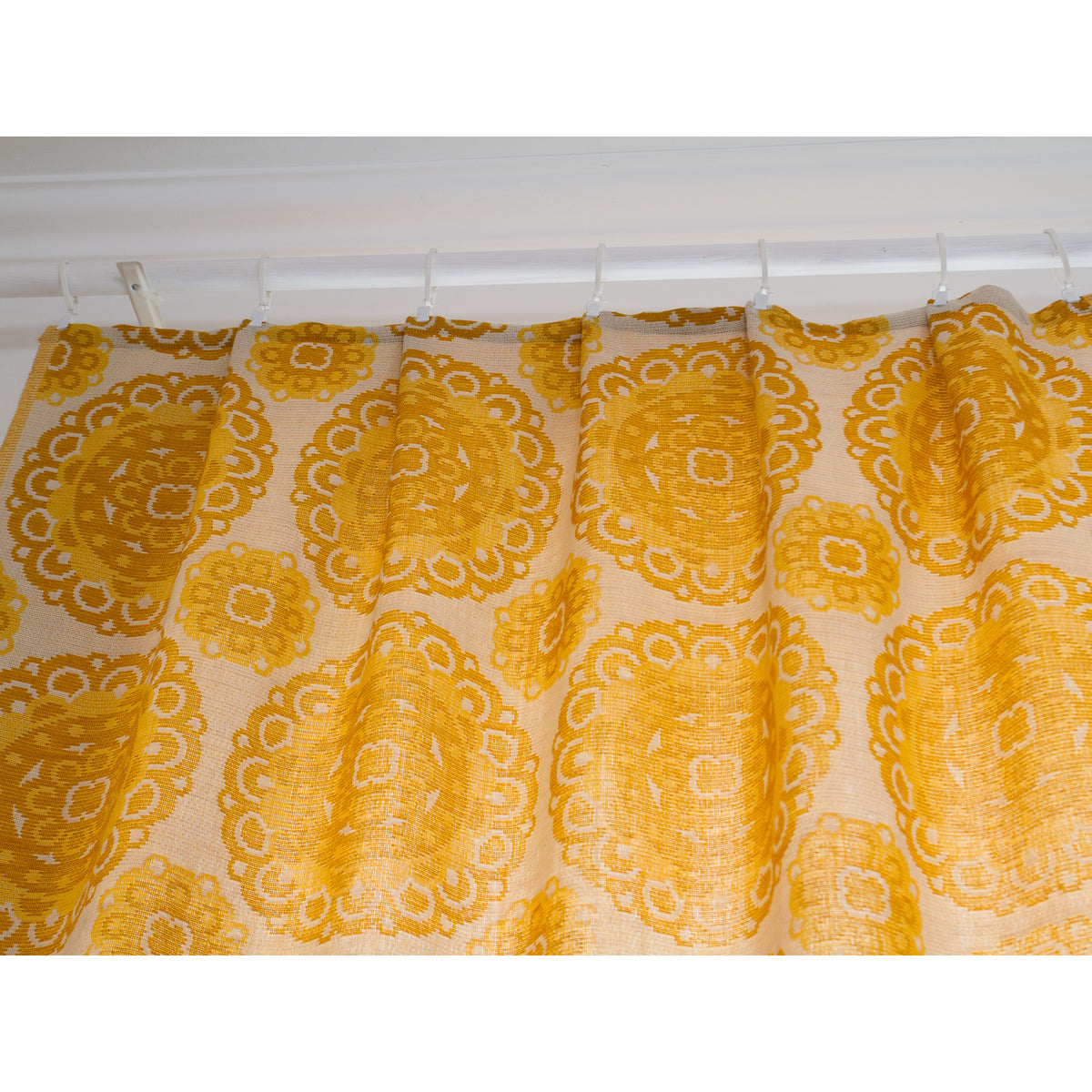 Top of vintage yellow drapes gathered with pleat tape and hanging on white curtain hooks