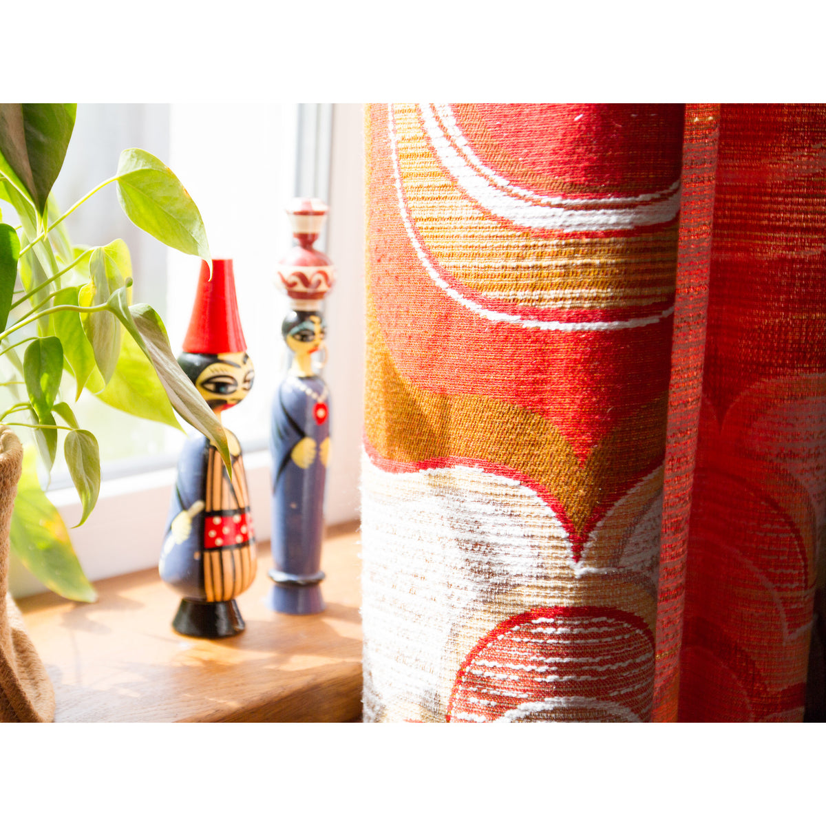 Detail of retro 70s curtain beside wooden folk figurines on a windowsill, warm orange and red colors