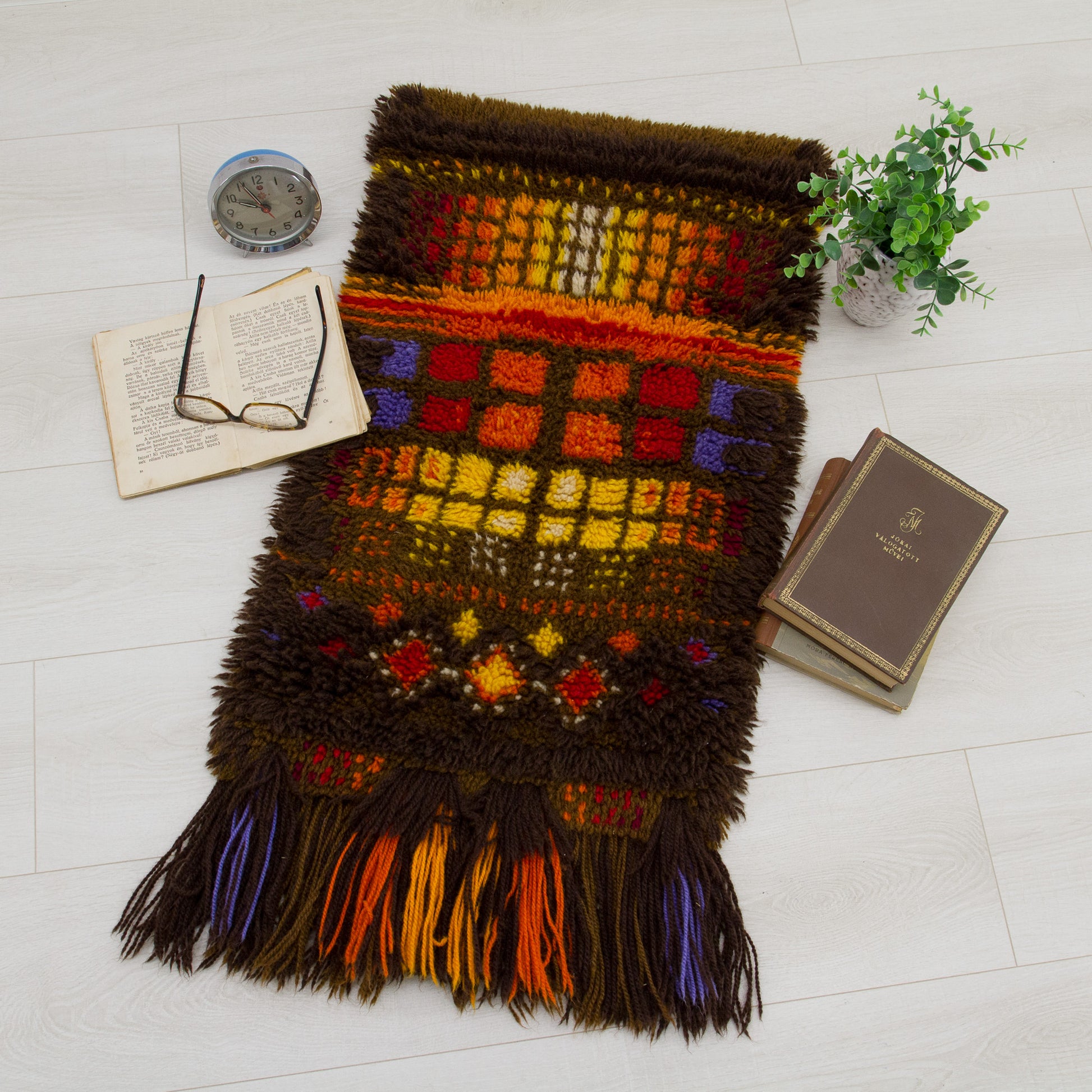 Top-down lifestyle view of the small, thick-pile vintage rug laid flat on the floor alongside retro books and an alarm clock to demonstrate scale and home aesthetic.