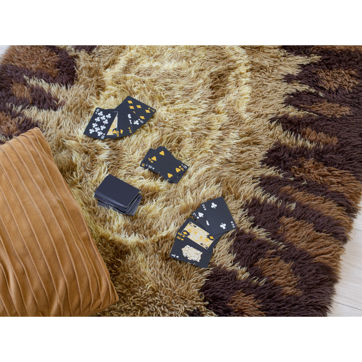 Retro 70s shag rug with vintage playing cards and a velvet cushion, relaxed lifestyle scene