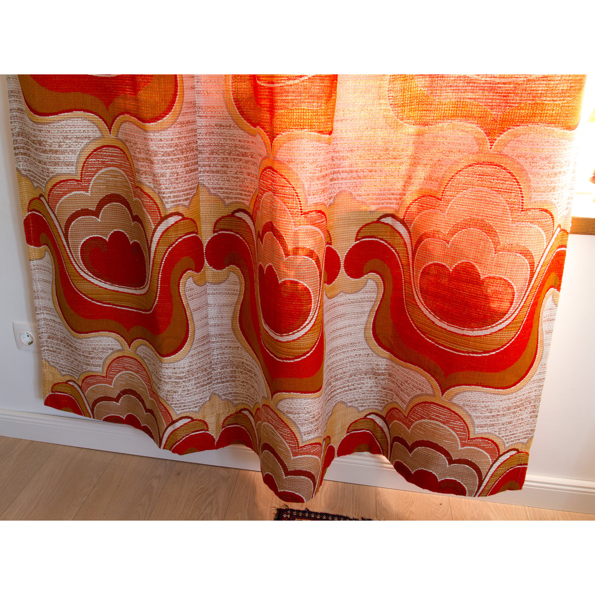 Full width of a retro woven curtain panel with repeating orange, red and cream flower shapes