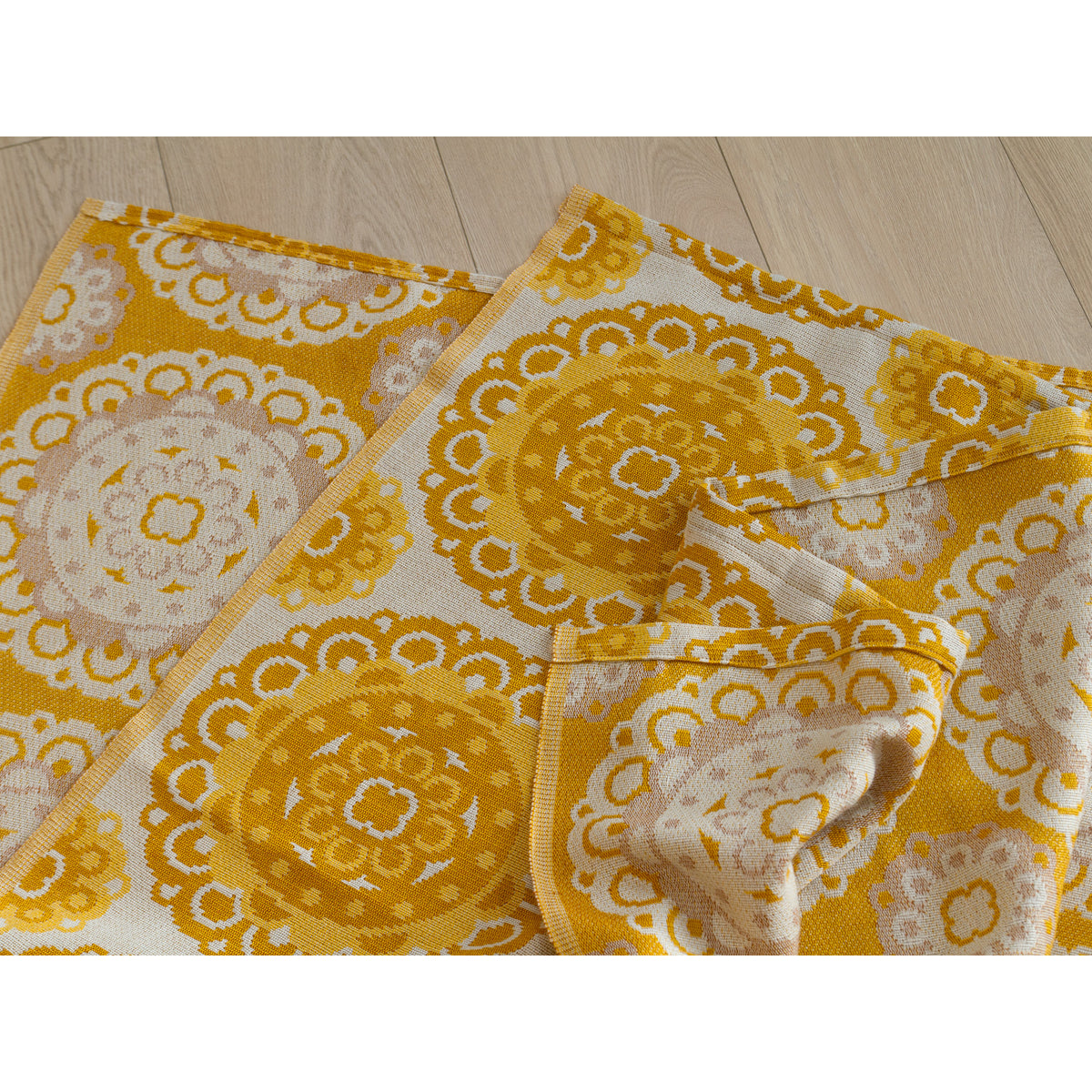 Closeup of the vintage jacquard drapes folded on a light wooden floor, showing yellow and cream reversible pattern.