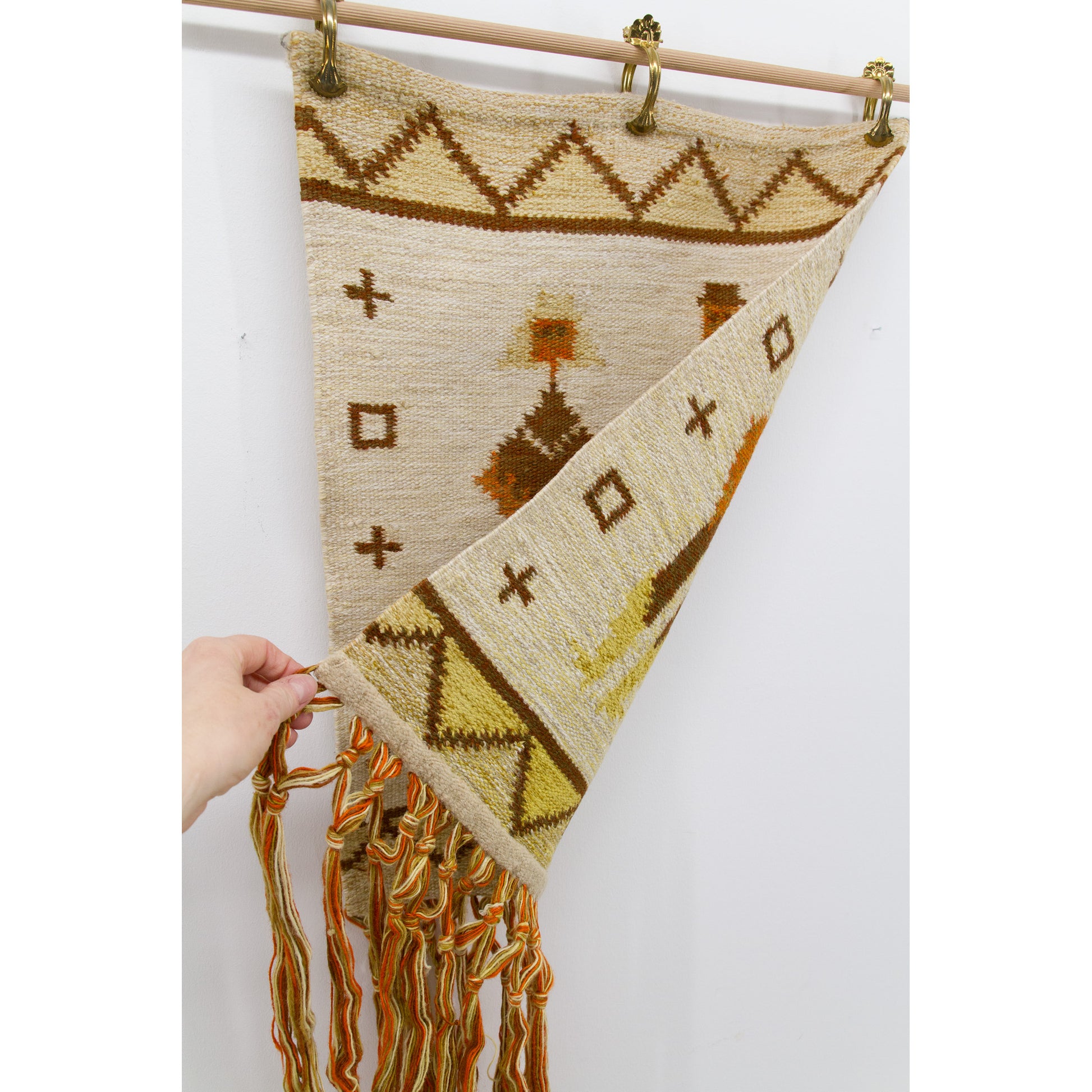 Hand lifting one bottom corner of the hanging vintage textile to reveal the perfectly identical, beautifully preserved and reversible back side.