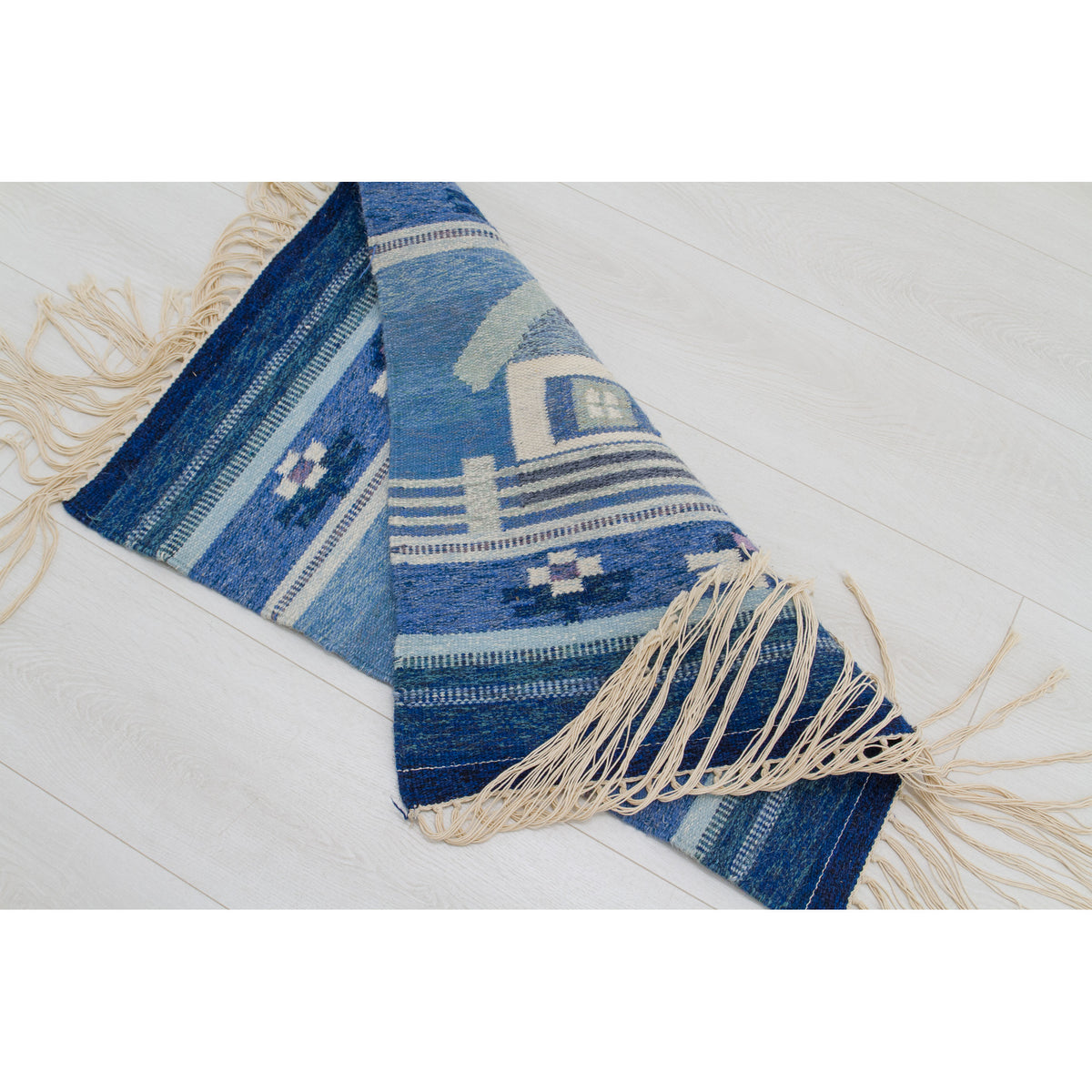 Full flat lay view on a white floor. Shades of navy, sky blue, and cream create a serene, wintery, or "Delft" color palette. Small reversible flatweave rug.