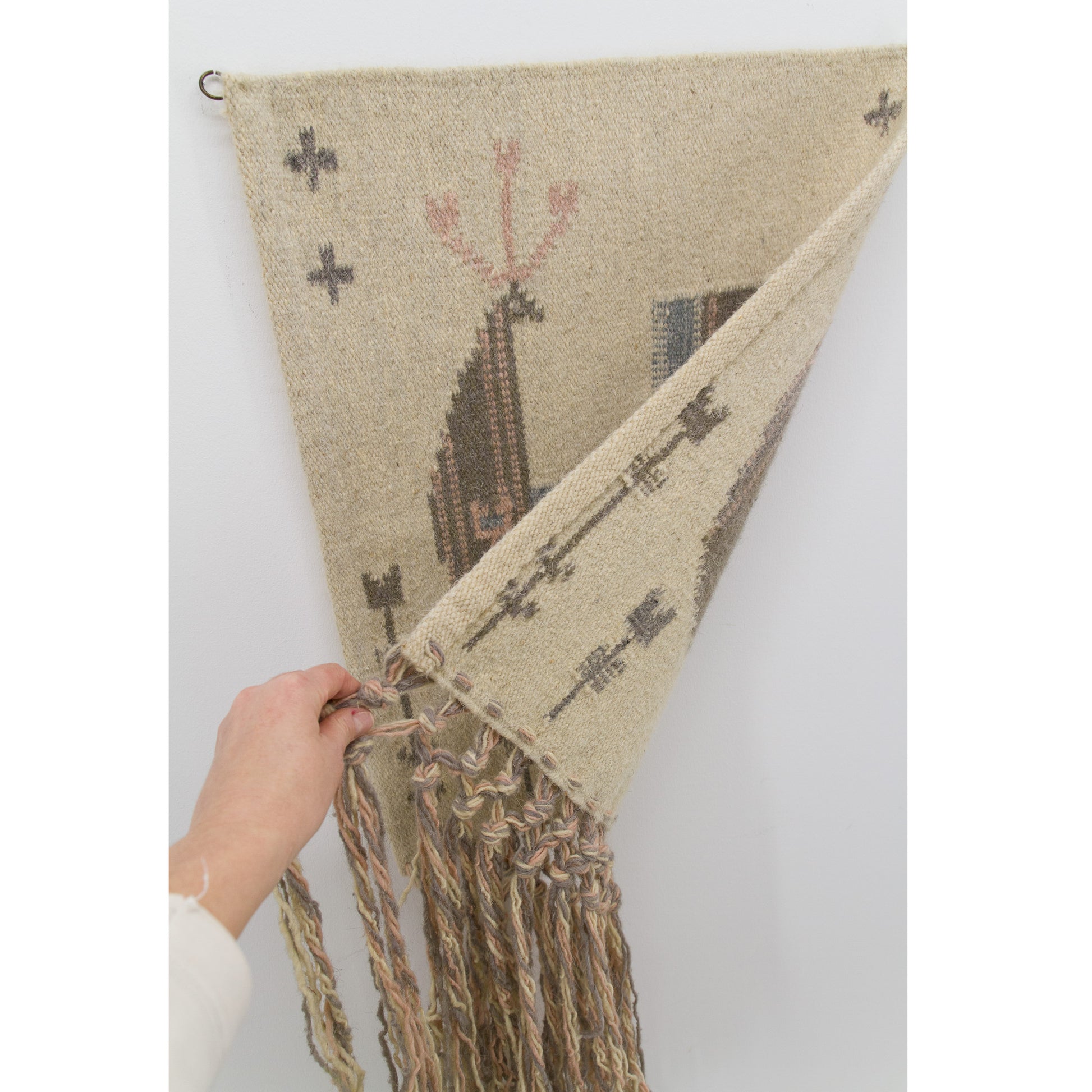 The textile hanging vertically as a hand softly folds up the lower corner, showcasing an immaculately finished edge and validating that the handwoven wool rug fabric is fully reversible.