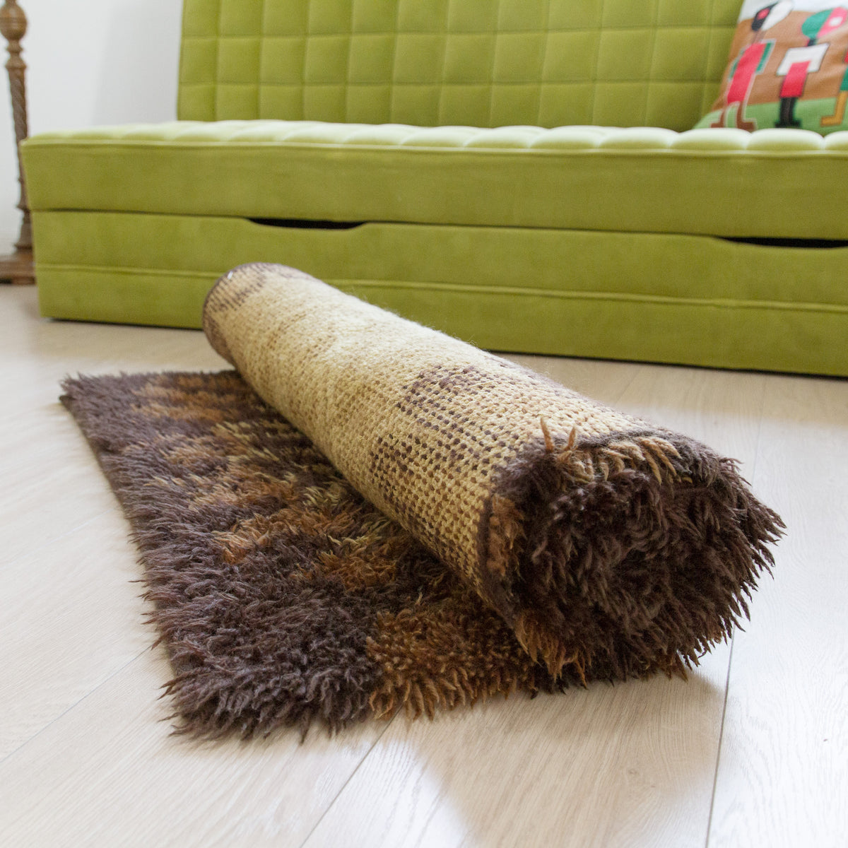 A rolled-up vintage rya rug in warm brown and beige dolors, displayed in a retro 1970s themed living room setting.